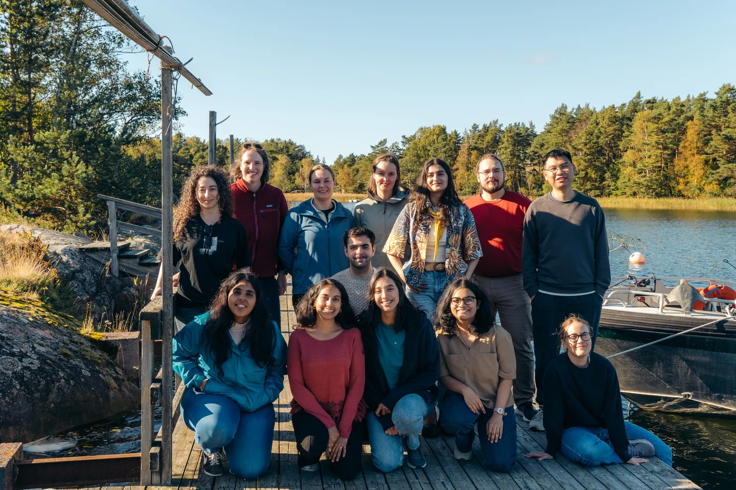 The group standing and sitting together on a wooden jetty beside the water and trees.