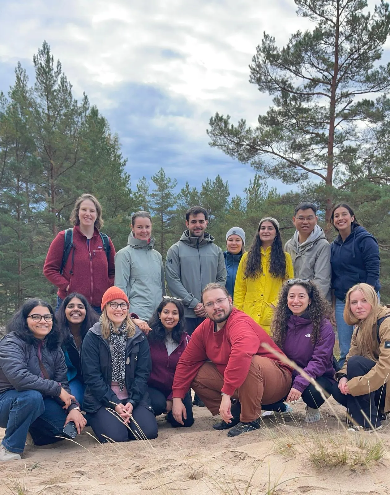 The group standing and kneeling together on a sandy path surrounded by pine trees.